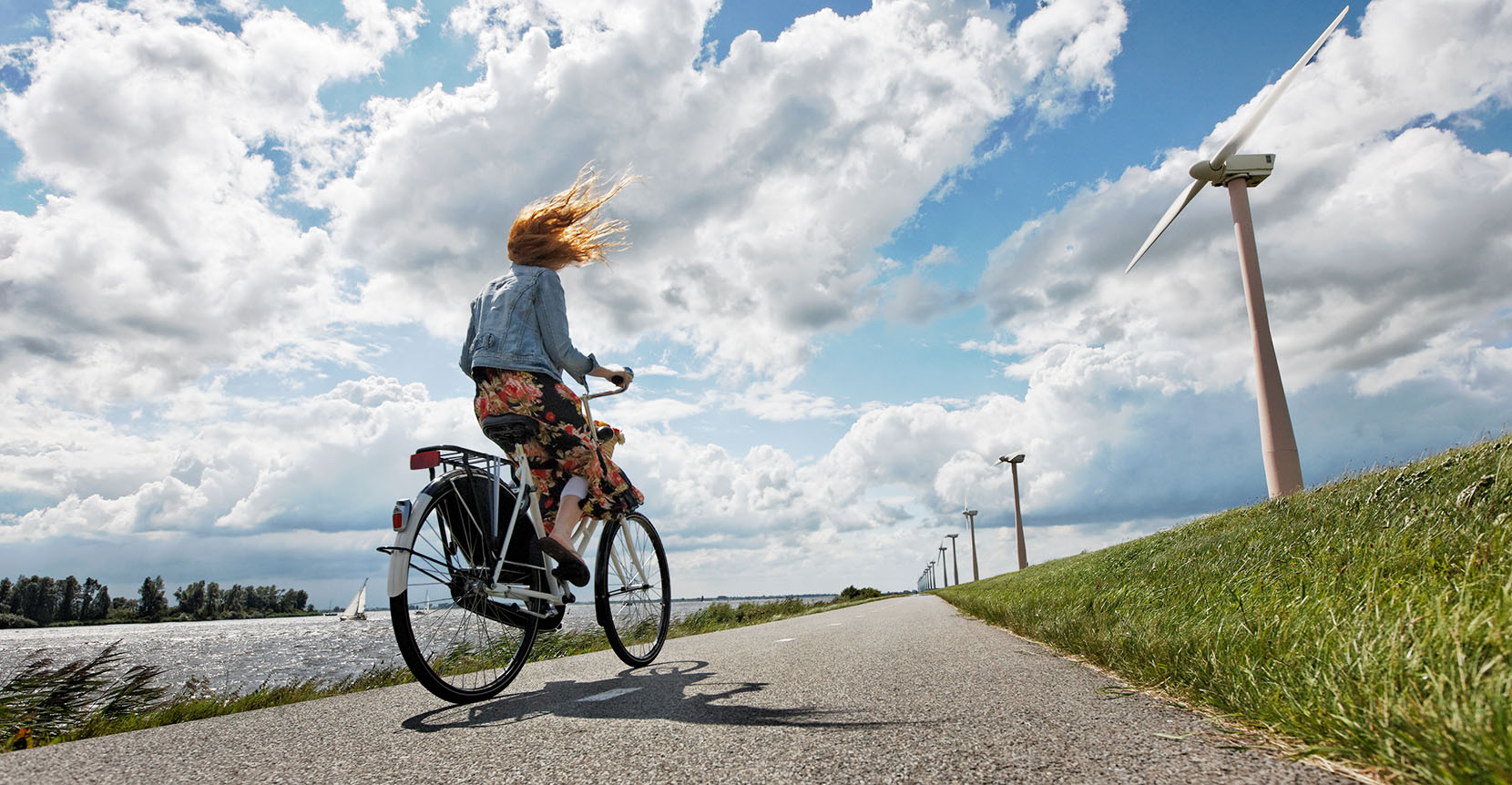 Vrouw rijdt met fiets op een weg met windmolens ernaast